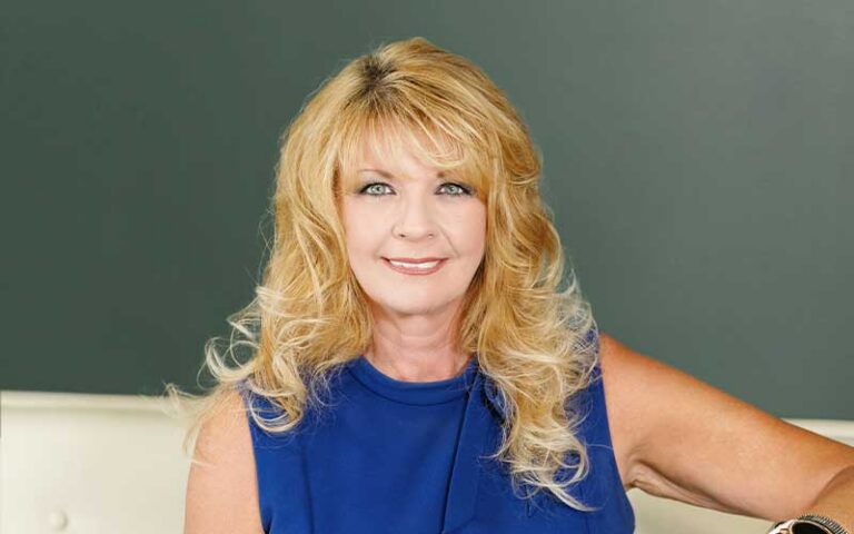 Professional headshot of a smiling blonde woman in a blue sleeveless top