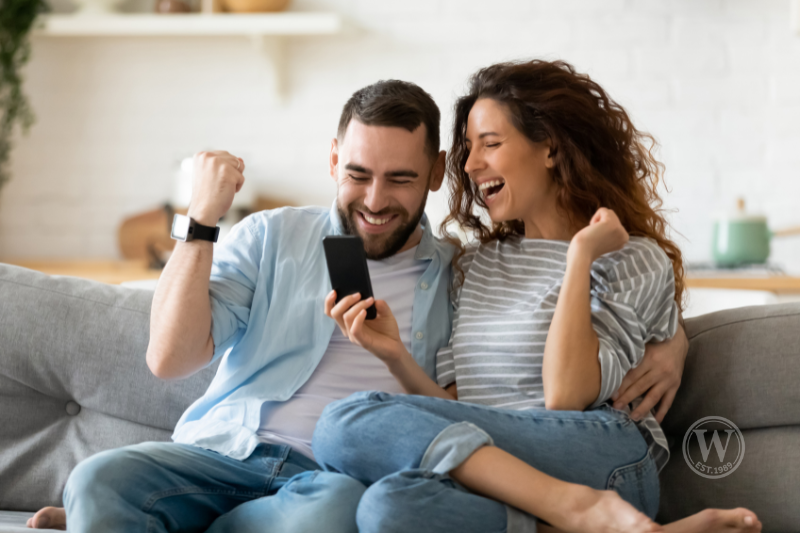 Happy couple celebrating good news on phone – Greater Fort Myers area homebuyers finding success.