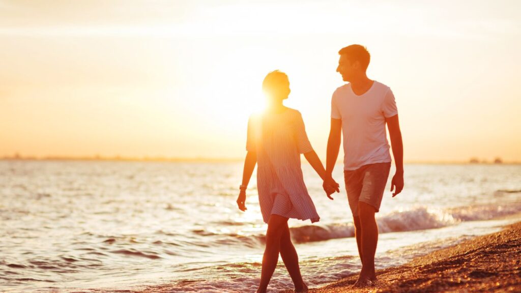 Couple walking along the beach at sunset with golden light reflecting on the Gulf of Mexico in Southwest Florida
