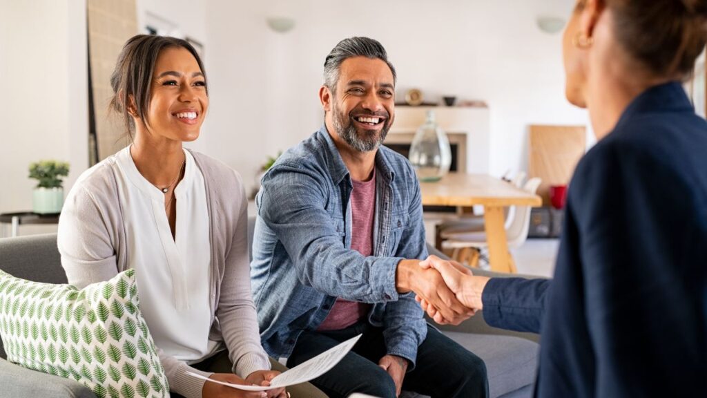 A smiling couple meeting with a real estate agent and shaking hands in their living room