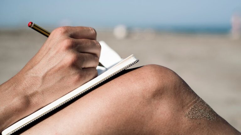 Person writing in a notebook while sitting on the beach, reflecting on their Fort Myers real estate career goals