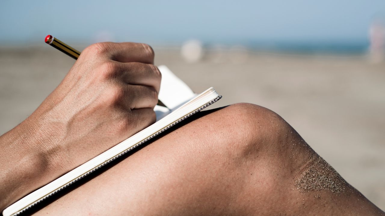 Person writing in a notebook while sitting on the beach, reflecting on their Fort Myers real estate career goals