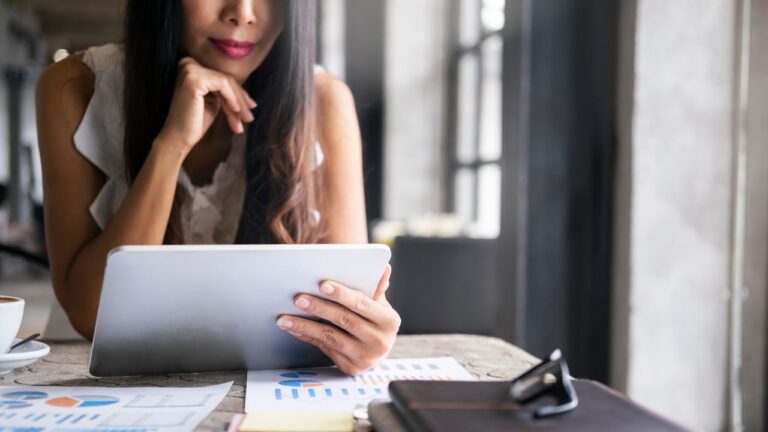 A woman reviewing housing market data on a tablet at a desk with charts and graphs
