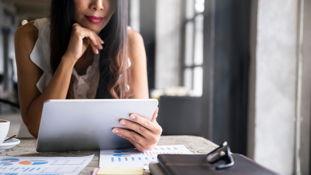A woman reviewing housing market data on a tablet at a desk with charts and graphs