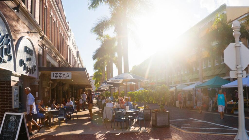 People dining outdoors and walking along brick streets in downtown Fort Myers, representing Lee County economic and housing trends