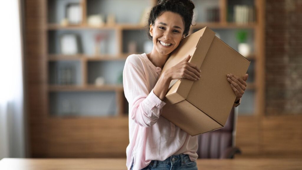 Smiling woman holding a moving box in her new home, symbolizing real estate as the best long-term investment