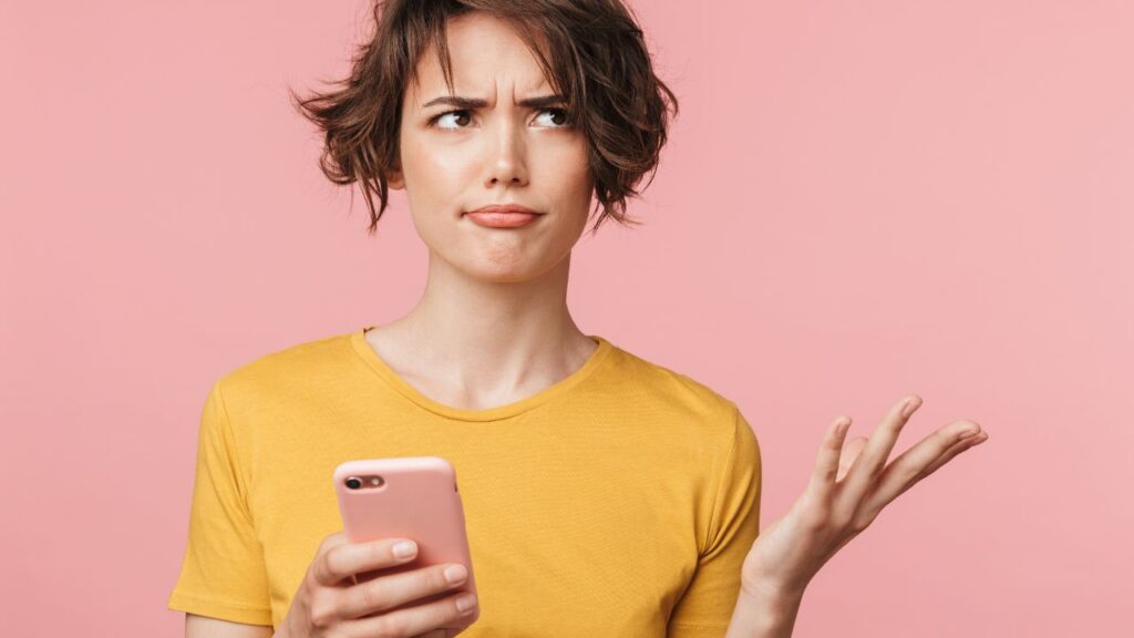 Confused young woman holding a phone against a pink background, representing the overwhelming nature of real estate news
