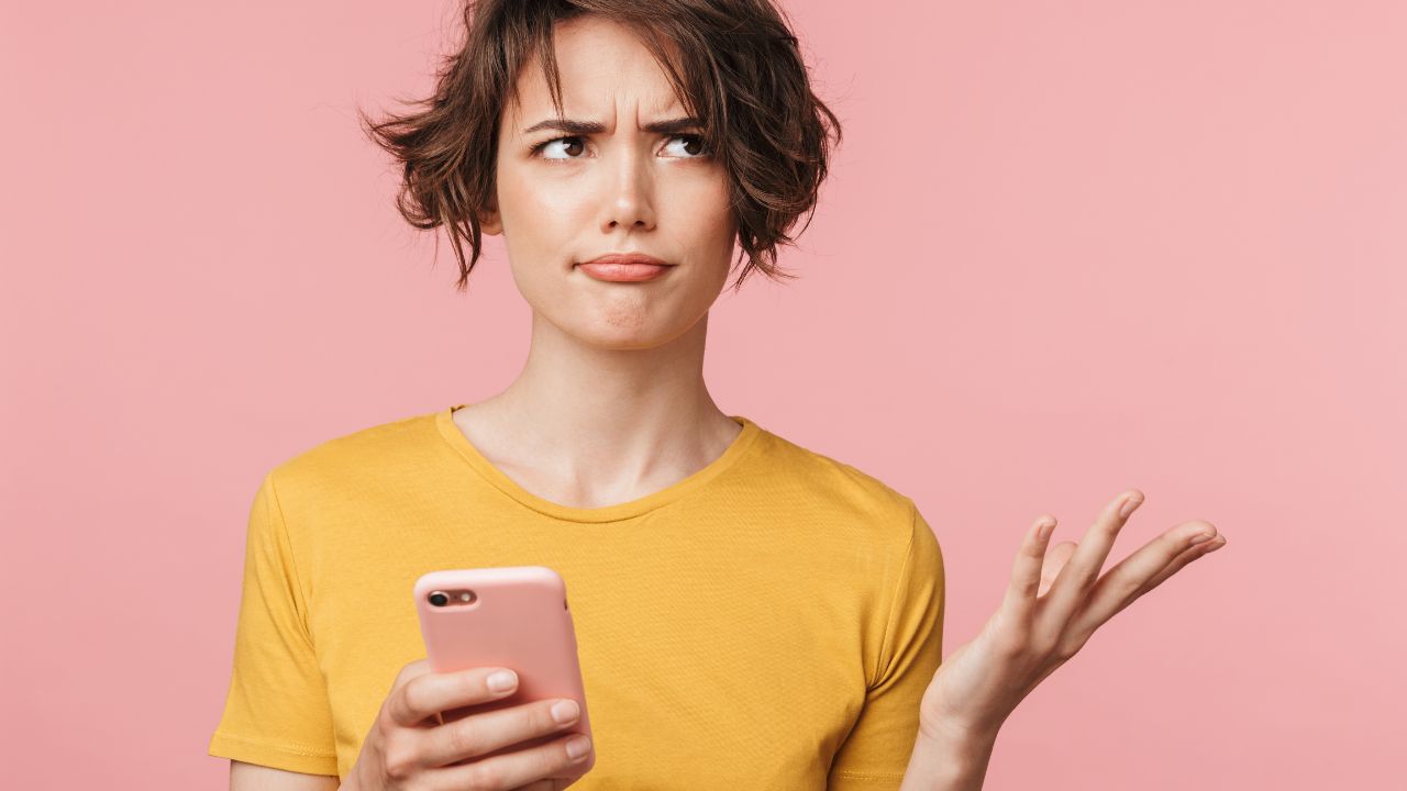 Confused young woman holding a phone against a pink background, representing the overwhelming nature of real estate news
