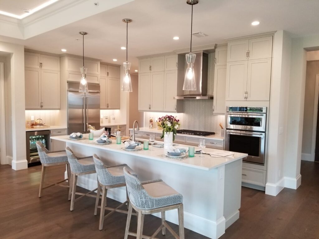 Bright Southwest Florida kitchen with white cabinetry, large island seating, pendant lighting, and wood flooring.