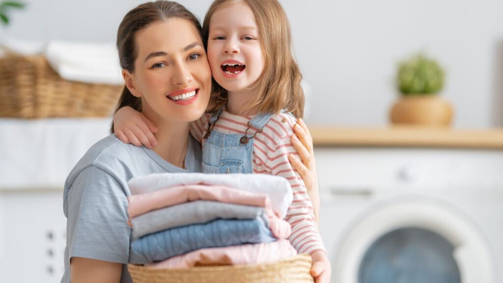 Smiling mother and daughter holding folded laundry, representing home safety and dryer vent cleaning in Fort Myers.