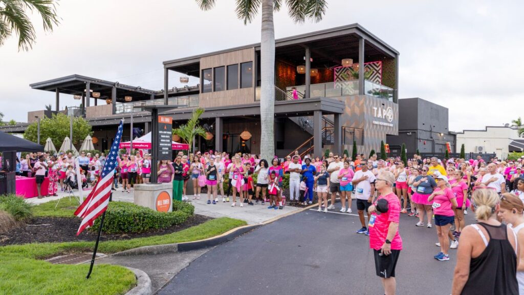 Runners and spectators stand for the national anthem outside Tap 42 at Bell Tower Shops before the Partners Pink Run Fort Myers 2025.