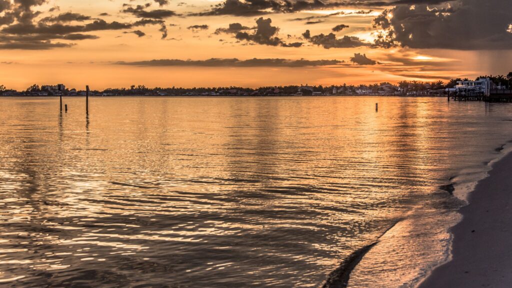 Sunset view over the Caloosahatchee River from Cape Coral Yacht Club Beach, showing calm water, shoreline, and waterfront homes that reflect the neighborhood’s coastal lifestyle.