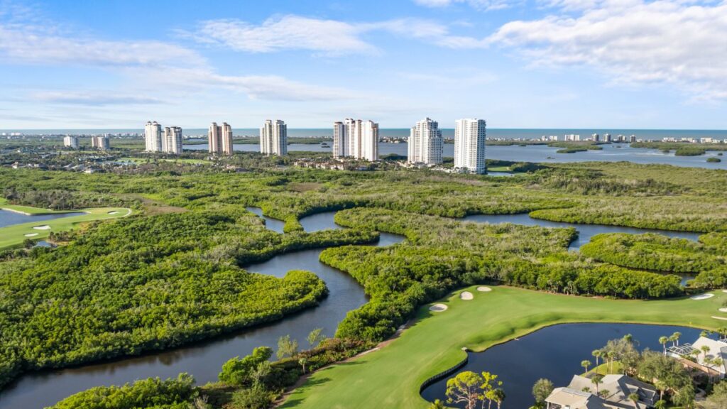 Aerial view of Pelican Landing in Bonita Springs showing the golf course, mangroves, and high-rise towers near the Gulf of Mexico.