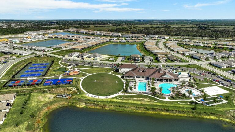 Aerial view of a master-planned community with clubhouse, pools, sports courts, lakes, and surrounding homes