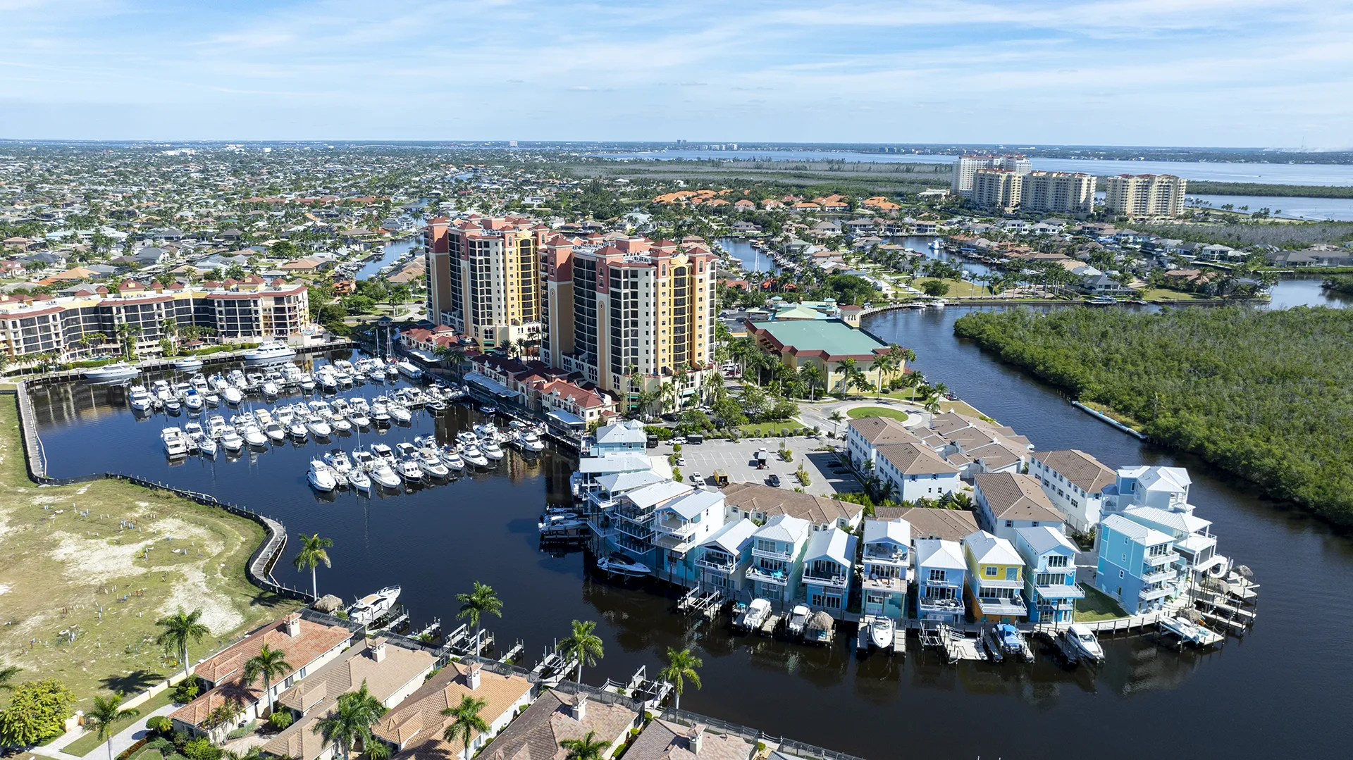Aerial view of Cape Harbour in Cape Coral, FL, featuring the full-service marina with boat slips, waterfront condo towers, townhomes with private docks, and direct Gulf access for homes for sale.