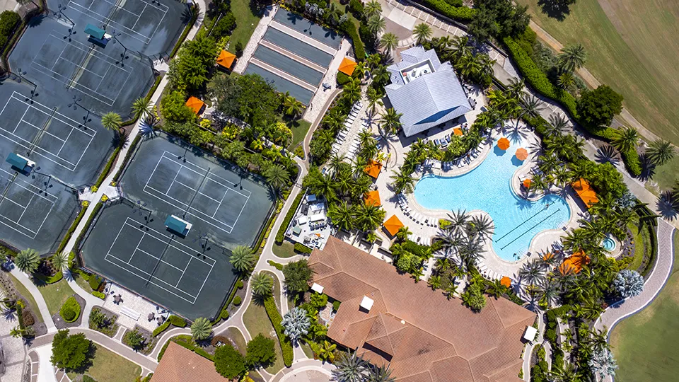 Aerial view of the resort-style pool, Har-Tru tennis courts, and pickleball courts at Esplanade Golf & Country Club of Naples, a bundled golf community with homes for sale in North Naples, FL