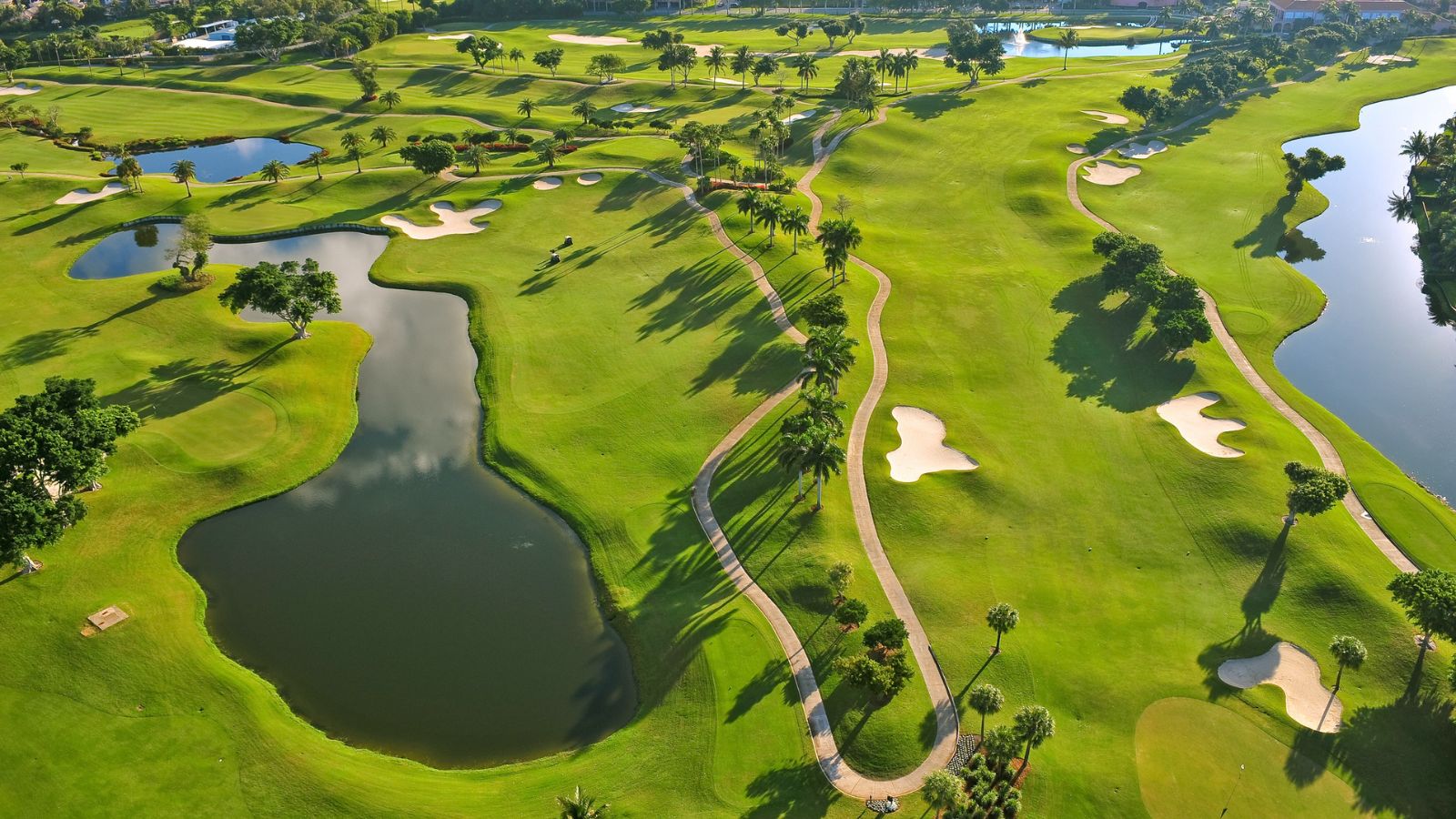Aerial view of an Estero, Florida golf course with lakes, fairways, and palm-lined cart paths at sunrise. Featured image for the Estero real estate market update.
