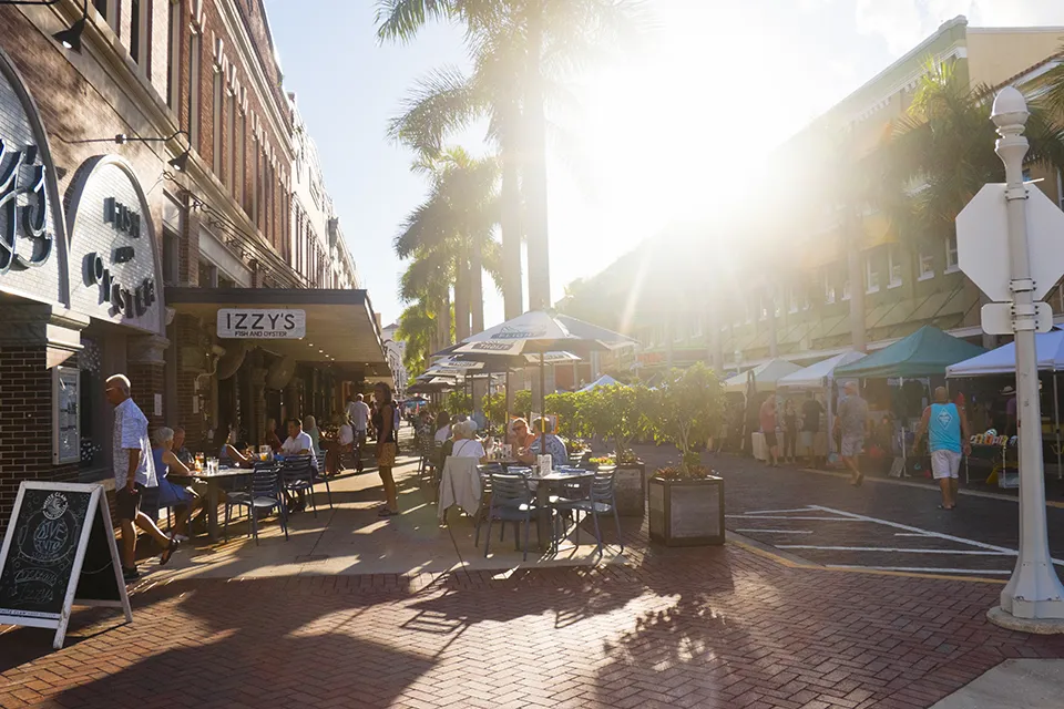 Outdoor dining and palm-lined streets in the Fort Myers River District, FL, with restaurants and pedestrians enjoying the sunny downtown atmosphere