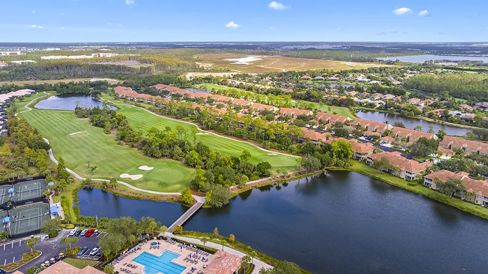 Aerial view of Grandezza Golf & Country Club amenities in Estero, FL, featuring the clubhouse, resort-style swimming pool, tennis courts, and adjacent 18-hole championship golf course with luxury homes for sale nearby.