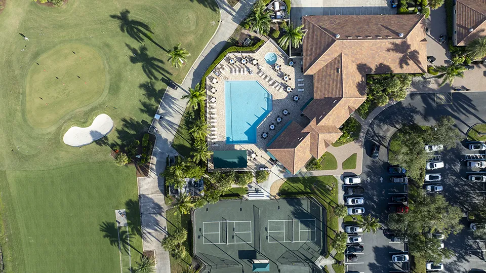 Aerial view of Lexington Country Club amenities in Fort Myers, FL, including the clubhouse, resort-style swimming pool, tennis courts, and adjacent bundled golf course with homes for sale nearby.