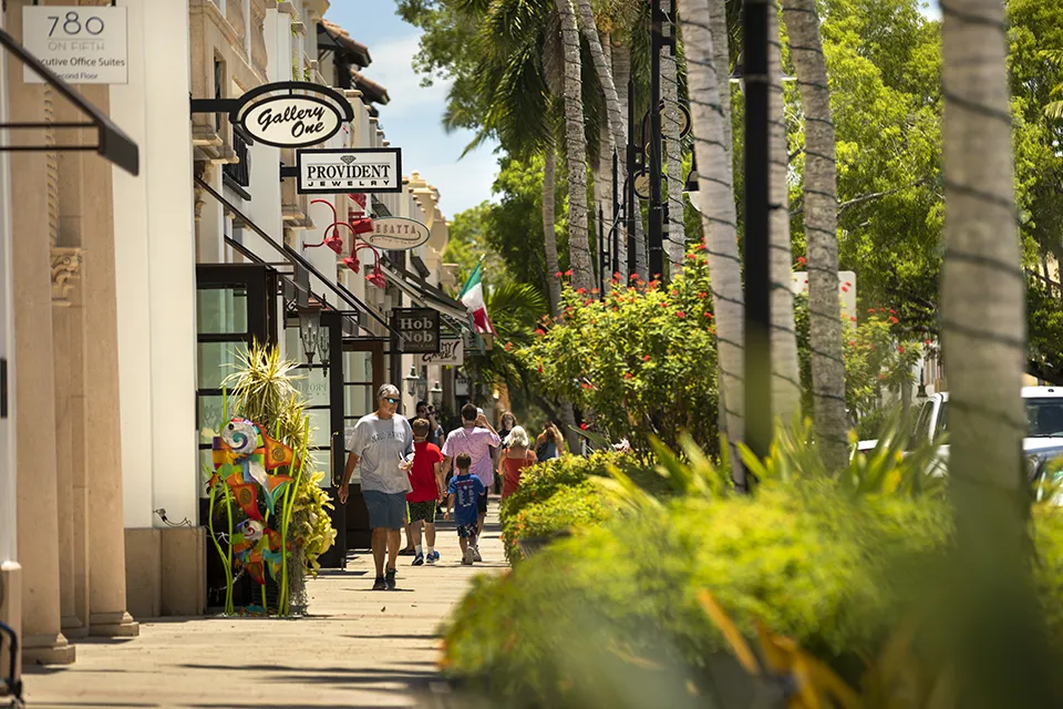 Pedestrians shopping and dining along palm-lined Fifth Avenue South in downtown Naples, FL, showcasing the area's upscale boutiques and restaurants