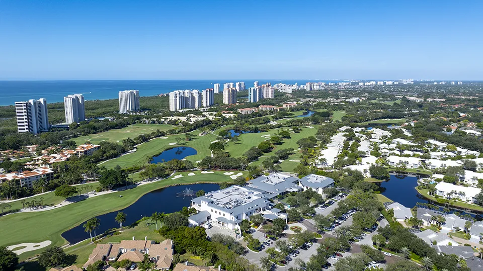 Aerial view of the Club Pelican Bay clubhouse overlooking lake and golf course at Pelican Bay, a luxury beachfront community with homes for sale in North Naples, FL