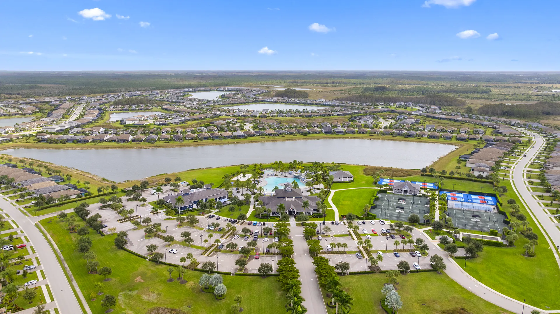 Aerial view of The Place at Corkscrew in Estero, FL, showcasing the gated master-planned community with lakes, resort-style clubhouse, pools with waterslide, pickleball courts, and single-family homes for sale.