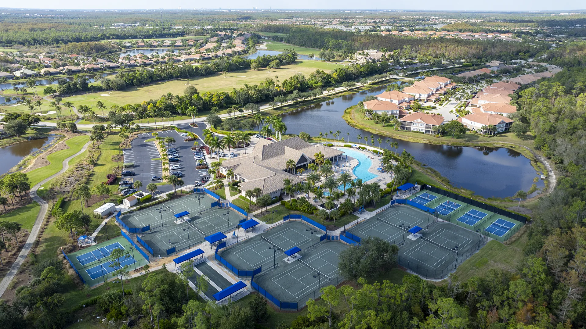 Aerial view of The Plantation in Fort Myers, FL, featuring the clubhouse, resort pool, tennis and pickleball courts, 18-hole championship golf course, lakes, and homes for sale.