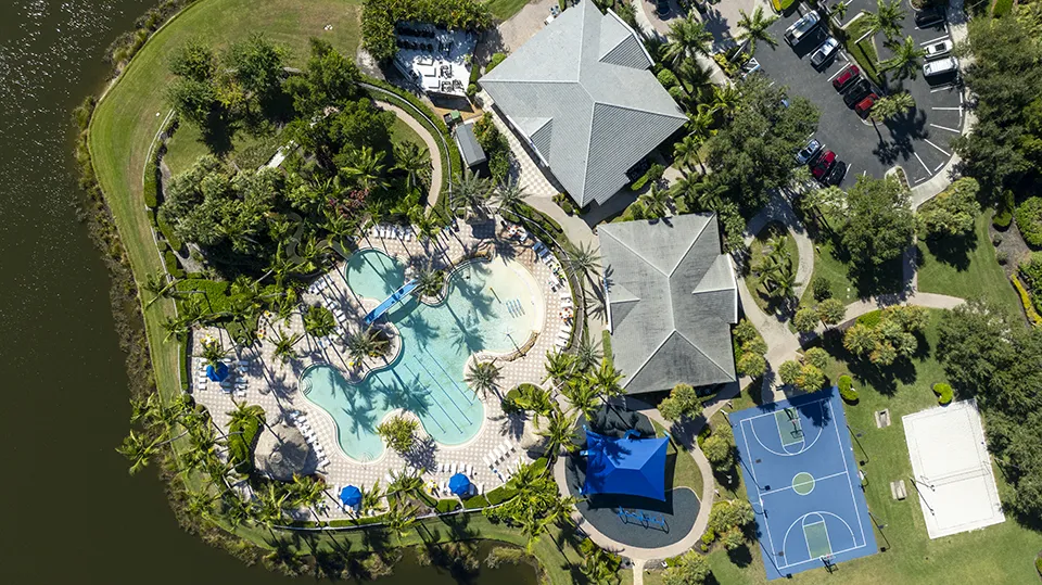 Aerial view of Sandoval amenities in Cape Coral, FL, featuring the clubhouse, resort-style lagoon pool with waterslide, tennis courts, basketball court, playground, and lakefront setting with homes for sale nearby.