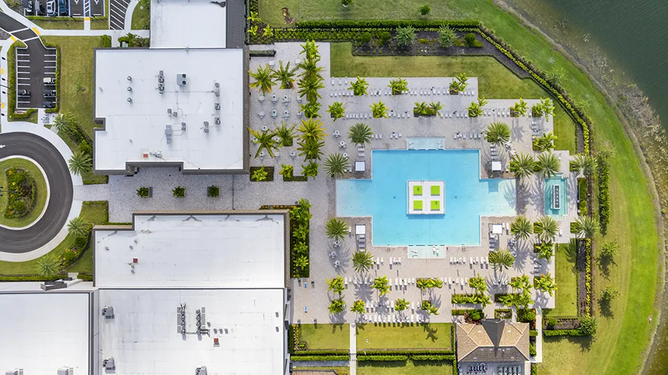 Aerial close-up of Verdana Village amenities in Estero, FL, featuring the clubhouse, resort-style swimming pool, tennis and pickleball courts, indoor sports complex, and lakefront setting with homes for sale nearby.