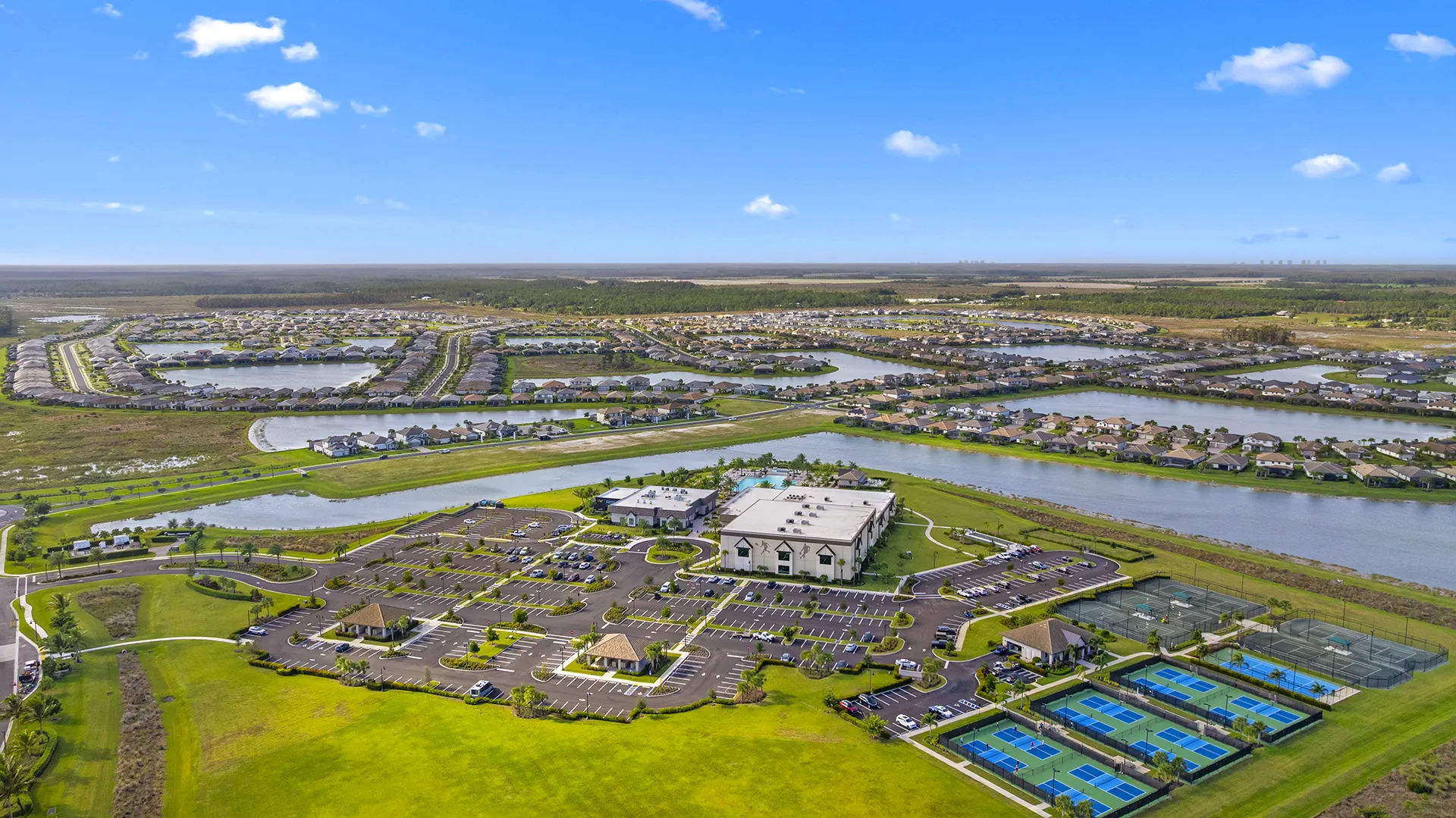Aerial view of Verdana Village in Estero, FL, showcasing the gated master-planned community with lakes, resort-style clubhouse, indoor sports complex, pickleball courts, and new homes for sale.