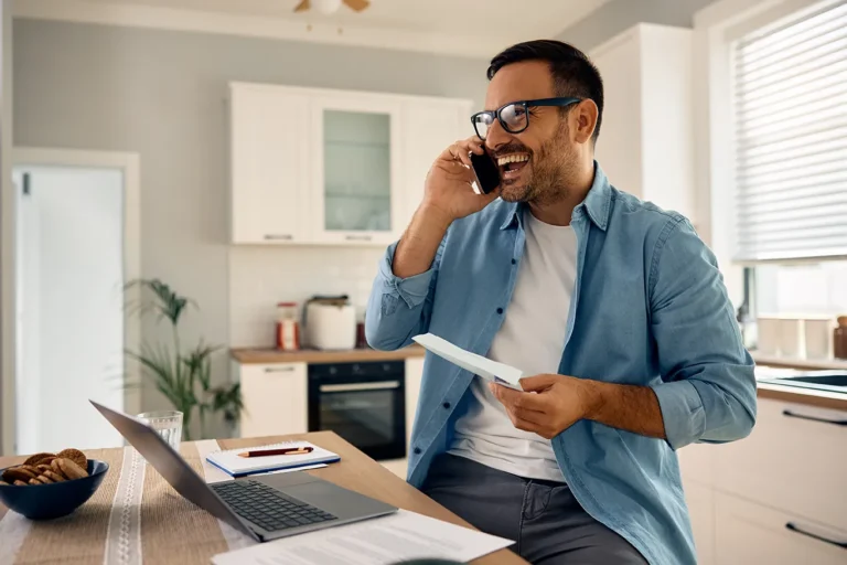 New real estate agent smiling on a phone call at a kitchen table while reconnecting with people in their sphere to find their first real estate clients