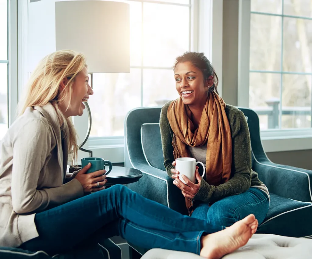 Two women having a relaxed conversation over coffee, representing the kind of genuine relationship that builds a real estate agent database