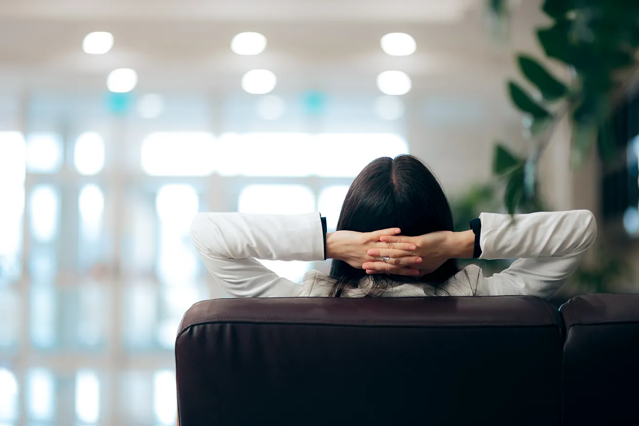 A professional woman leans back comfortably in a modern office, hands behind her head, relaxed and confident in her environment
