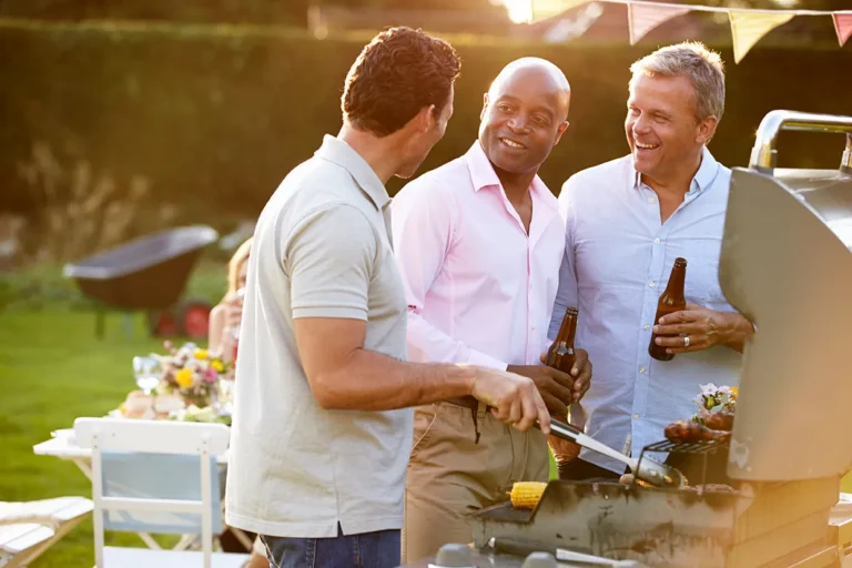 Three neighbors laughing and talking at a backyard cookout, illustrating how real estate careers are built through personal conversations without social media