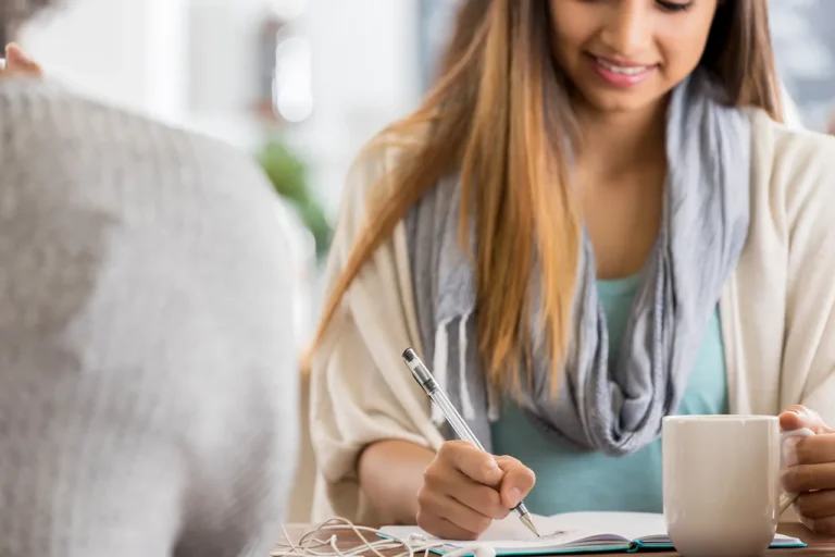 Real estate agent writing handwritten thank you note at coffee shop—a successful real estate agent habit that compounds over time