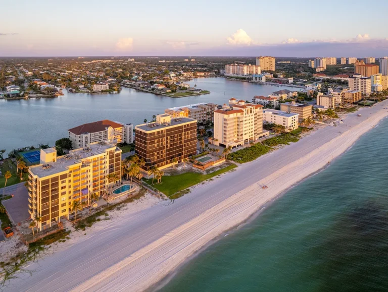 Aerial sunset view of Gulf Shore Drive in Naples, Florida, with beachfront condos lining the Gulf of Mexico and Vanderbilt Lagoon on the bay side.