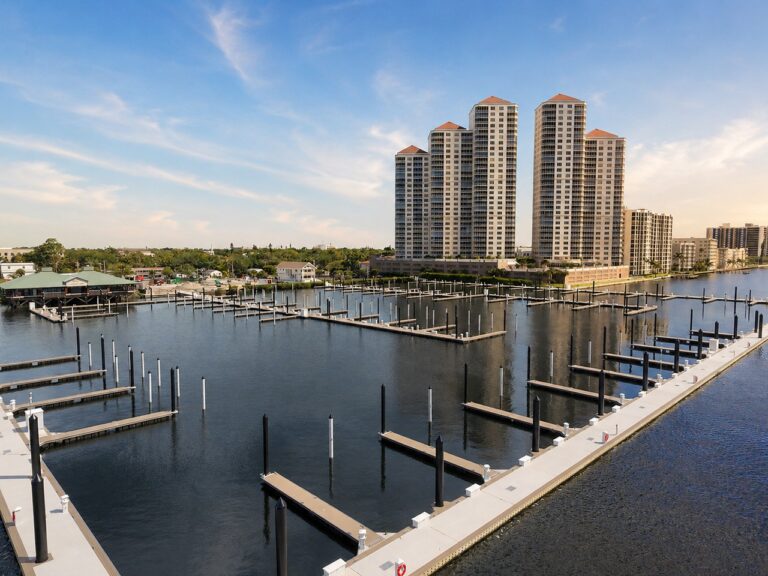 Waterfront condo towers overlooking a marina with empty boat slips under a blue evening sky