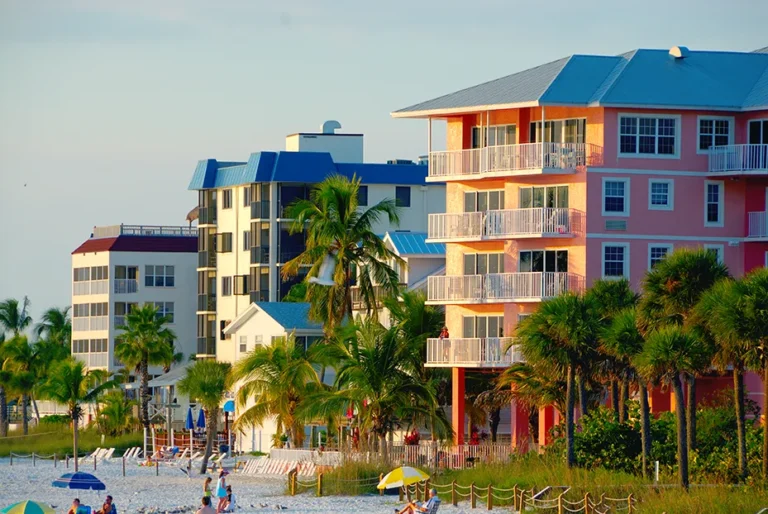 Colorful beachfront condos with balconies, palm trees, and a sandy beach at sunset