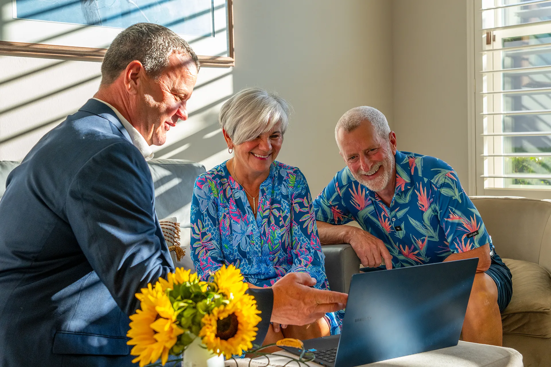 Real estate agent reviewing options on a laptop with a smiling couple in a bright living room