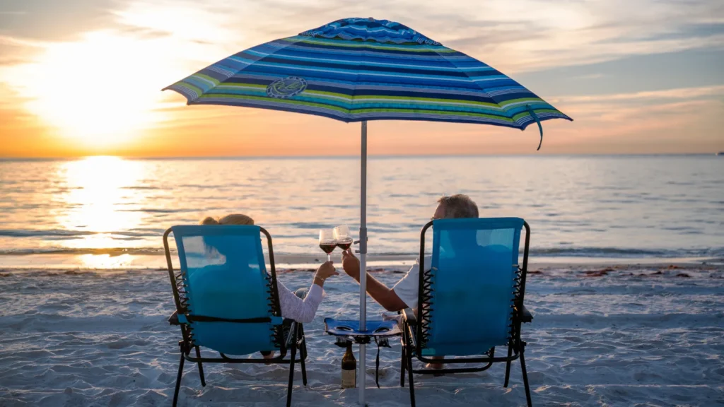Couple toasting wine in beach chairs at sunset on Vanderbilt Beach in Naples, Florida, the lifestyle behind a move from Naperville to Naples.