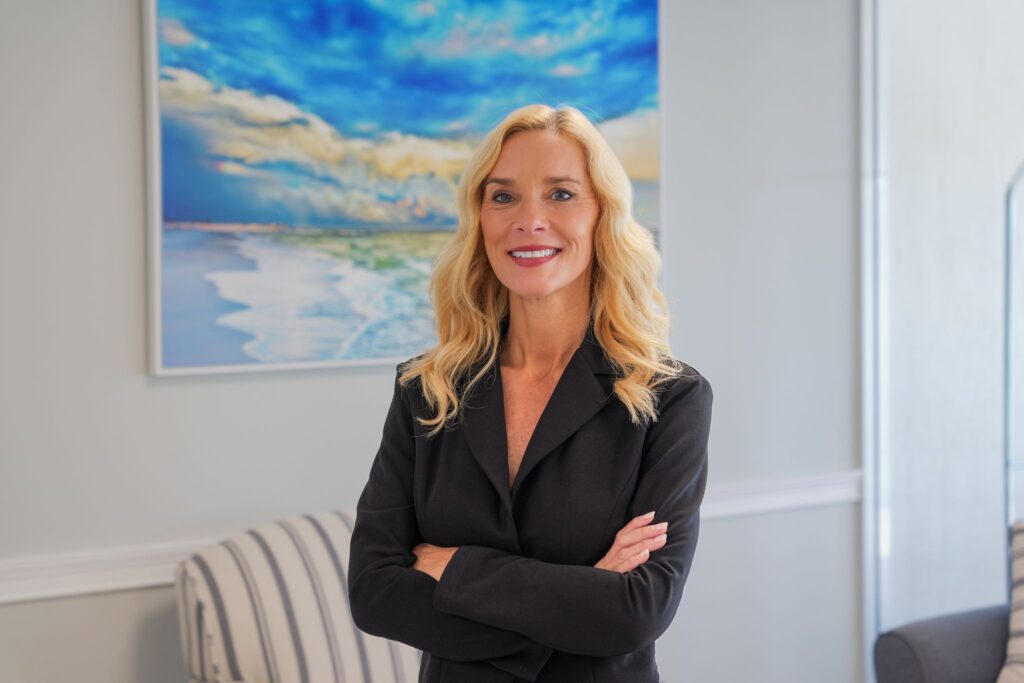 Amy Fossett, North Naples Realtor with Worthington Realty, standing with her arms crossed in a bright coastal interior.